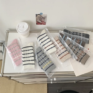 Detailed view of striped crew socks in pink and grey tones, neatly packed in branded zip bags