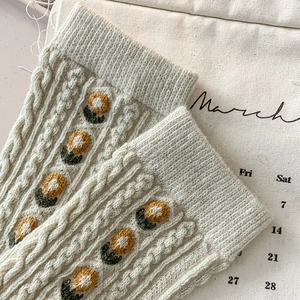 Macro detail of creamy white wool socks featuring floral embroidery and cable knit texture