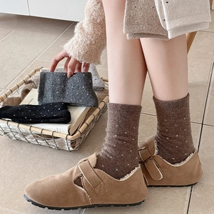 Detail of wool polka dot socks paired with buckle shearling sandals in warm indoor setting