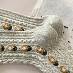 Close-up of thick cable-knit wool socks featuring colorful floral embroidery details