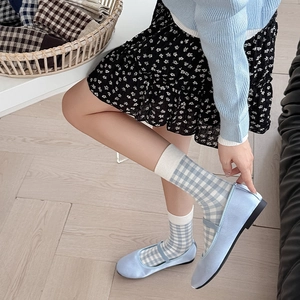 Detail shot of light blue Mary Jane flats worn with blue plaid crew socks in a cozy setting