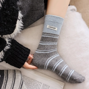 Close-up of blue and gray striped knitted crew socks with a fabric label on a white rug