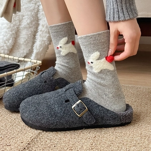 Detail of wool socks with white rabbit embroidery and red pom-poms worn with gray clogs
