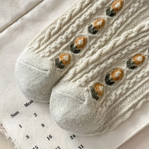 Close-up of beige cable knit wool socks featuring delicate yellow and green floral embroidery