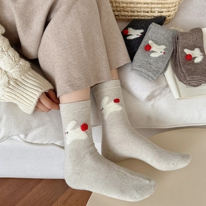 Close-up of thick knitted wool socks with 3D bunny patterns and cute red pom-poms