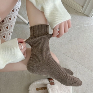 Detail of hand stretching a brown ribbed wool sock to show high elasticity and thickness