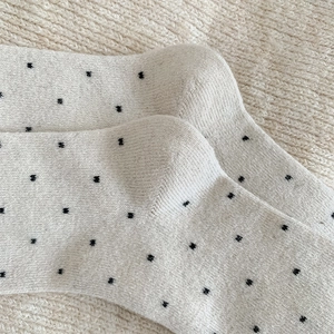 Close-up of cream knit socks with black polka dots on a soft woolen background