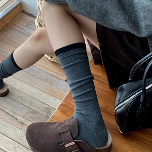Detail of dark gray knitted calf socks with black trim styled with suede clogs and skirt