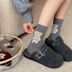 Close-up of cozy grey wool socks with cute bear pattern and felt mule slippers on rug