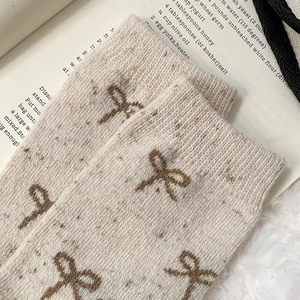 Close-up of thick knit beige socks with tweed texture and brown bow detailing