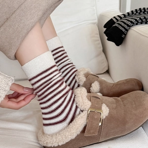 Detail of warm striped wool socks paired with brown suede clogs on a soft sofa