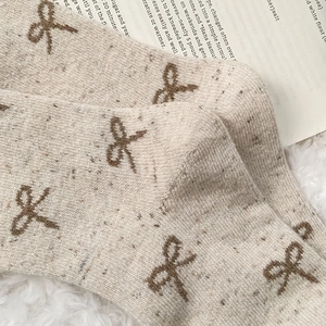 Close-up of beige wool knit socks with brown bow embroidery and speckled texture detail