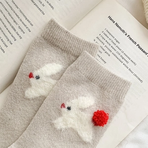 Detailed knit of warm wool sock featuring 3D fuzzy rabbit and red pompom on beige fabric