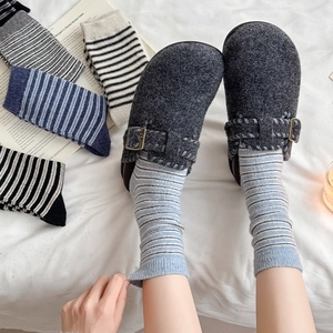 Detail of dark grey felt clogs with metal buckles paired with striped wool knit socks