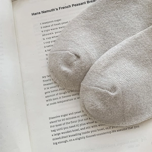 Gros plan d'une chaussette épaisse en laine tricotée grise posée sur un livre ancien