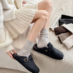 Close-up of cozy grey felt clogs with wool socks on a soft white checkered bedsheet