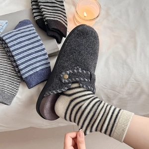 Detail of wool felt clogs with stitching and striped knit crew socks in a cozy setting