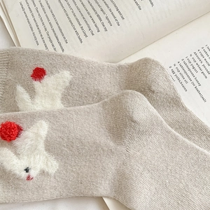 Detailed knit texture of beige bunny wool socks with 3D white fur and red pom-poms