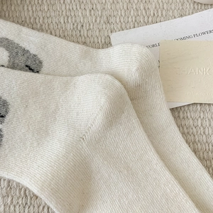 Detail of cream knit crew socks with vertical rib texture and cute grey panda pattern