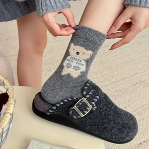 Cute gray cartoon bear wool socks and dark gray wool felt mule slippers on light carpet