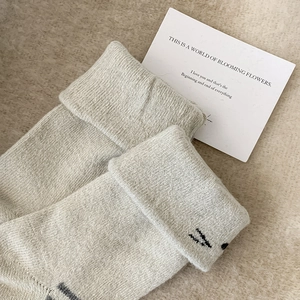 Detailed close-up of cream knit socks with cute cat embroidery and folded cuffs