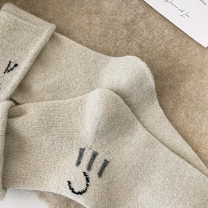 Detail of oatmeal knit wool socks featuring a minimalist embroidered winking cat face