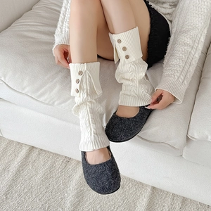 Detailed knit texture of beige leg warmers featuring cable patterns and wooden buttons