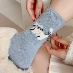 Close-up of light blue knit socks featuring a cute white cat and plaid bow detail
