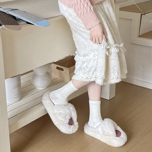Close-up of cream fuzzy cross-band slippers with plush texture in a home setting