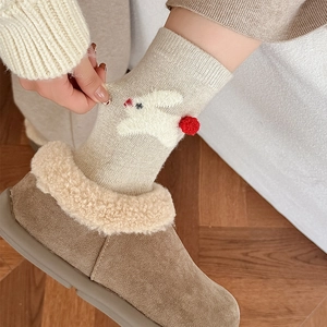 Close-up of oatmeal knit socks with white rabbit embroidery and red pom-pom details