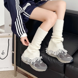 Close-up of white knitted leg warmers with grey fringe detail and chunky yarn texture