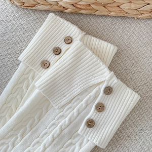 Close-up of cable knit leg warmers with vintage buttons and ribbed cuffs in off-white
