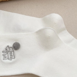 Nahaufnahme weißer Rippsocken mit grauen Bommeln und feinen Stickerei-Details