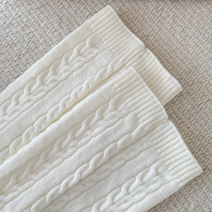 Detailed cable knit pattern on off-white leg warmers with ribbed texture and soft finish