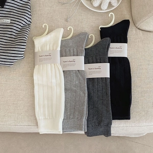 Detail of ribbed knit socks in white, grey, and black with brand paper packaging