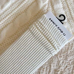 Close-up of white ribbed knit crew socks with brand packaging on knit texture
