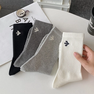 Detail of ribbed knit texture and embroidered logo on mid-calf socks in neutral tones