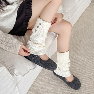 Detail of cream knit leg warmers featuring cable texture and wooden button accents