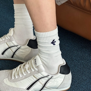 Detail of white ribbed mid-calf socks featuring blue embroidered arrow logo with sneakers