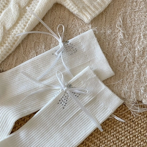 Detailed knit texture of white calf socks with ribbon bows and rhinestone accents