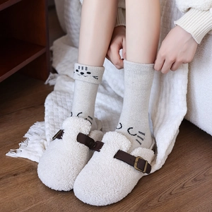 Cozy white faux shearling clogs with gray cartoon cat wool socks on a wooden floor