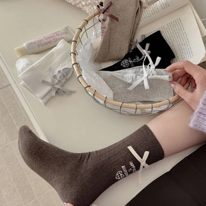 Close-up of knit mid-calf socks featuring 3D ribbon bows and heart letter embroidery