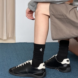 Detail of black mid-calf cotton socks featuring white wing embroidery and ribbed cuffs