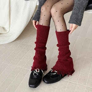 Close-up of deep red knitted leg warmers with distressed tassel hem and thick texture