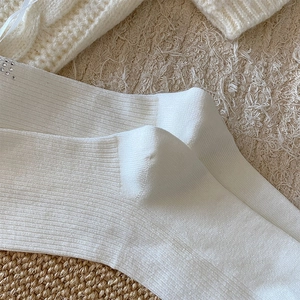 Close-up of white ribbed knit socks featuring delicate rhinestone bow embellishments