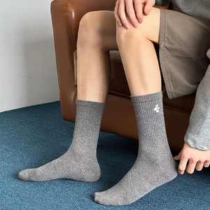 Grey ribbed mid-calf sports socks with white side embroidery worn in a casual indoor setting