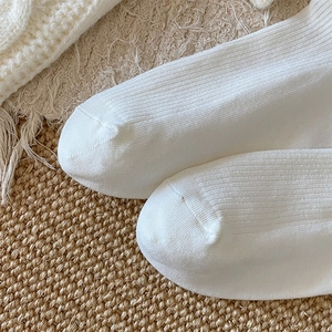 Close-up of white ribbed knit socks toe stitching detail on textured background
