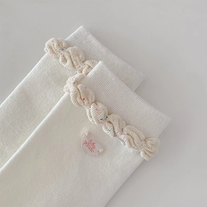 Detail of white knit socks with colorful flecks, twisted ruffle cuffs and a heart tag