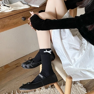 Detail of black knit mid-calf socks with white satin bows and ballet flats in retro style