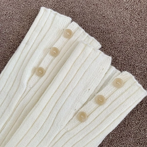 Close-up of white ribbed knit leg warmers featuring button slit detail and soft texture